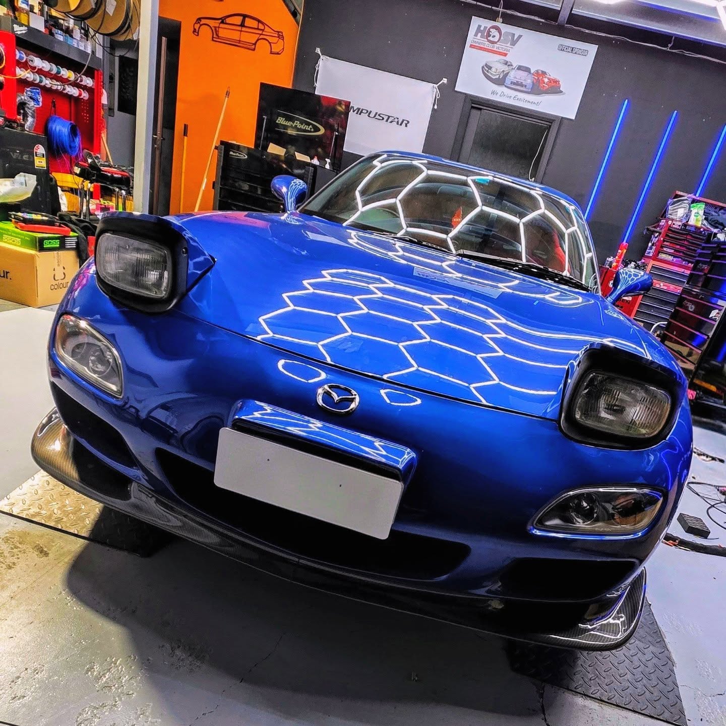 Blue Mazda RX-7 FD under the workshop hex lighting
